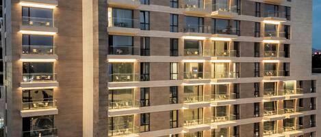A modern hotel building with multiple balconies, a well-lit entrance, and a landscaped courtyard.