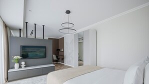 A modern bedroom with a large bed, a TV mounted on the wall, and a console table with a vase of flowers. - ONE66 (Brașov)