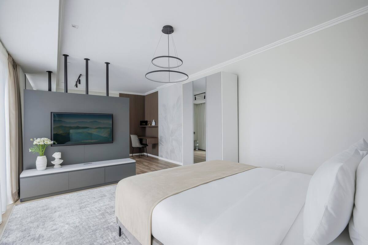 Un dormitorio moderno con una cama grande, un televisor en la pared y una mesita de consola con un florero.