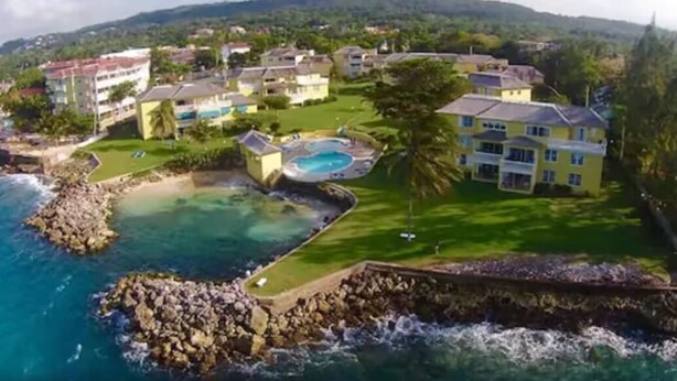 A coastal resort with multiple buildings, a swimming pool, and a rocky shoreline.