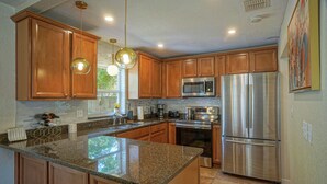 A kitchen with wooden cabinets, stainless steel appliances, granite countertops, pendant lighting, and a tiled backsplash.