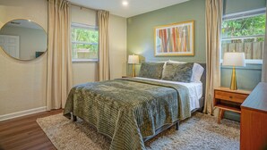 A bedroom with a bed, two bedside tables, a mirror, and a window with curtains.