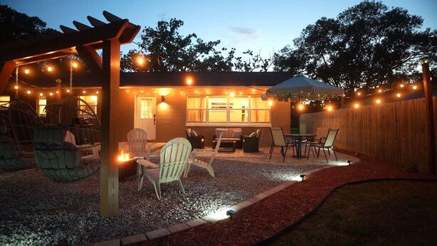 A backyard with a pergola, string lights, a fire pit, outdoor furniture, and a wooden fence.