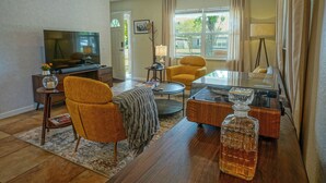 A living room with a television, a yellow armchair, a coffee table, and a glass decanter on a wooden table.