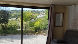 A room with a large sliding glass door leading to a gravel driveway, a grey sofa, a patterned rug, and a ceiling light fixture. - Lovely apartment with swimming pool and exterior (Gabian)