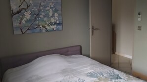 A bedroom with a bed, a door, a wall-mounted painting, and a hanging light fixture. - Lovely apartment with swimming pool and exterior (Gabian)