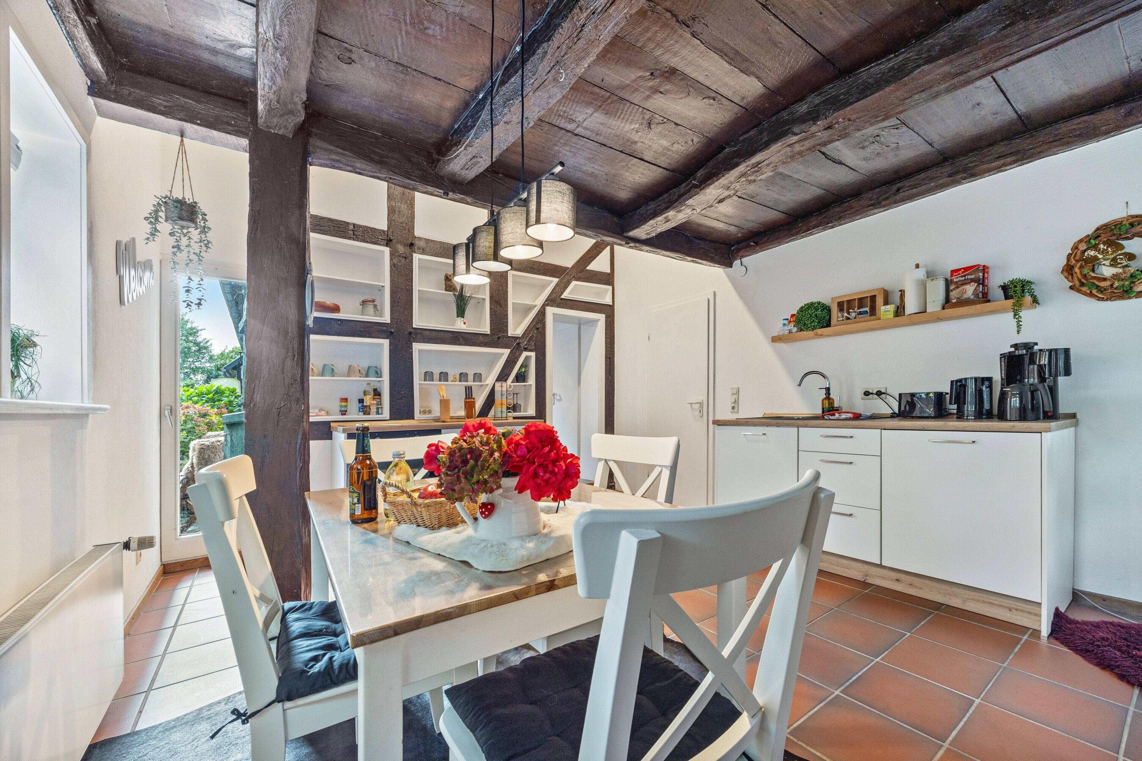 Une cuisine avec des meubles blancs, un plafond en bois et un coin repas comprenant une table et des chaises.