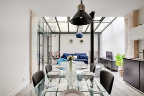 A modern dining area with a glass table, chairs, and a hanging light fixture. - Elegant Apartment -2br/4p - Sacre-coeur (Paris)