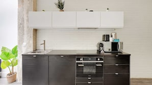 A kitchen with a white backsplash, dark cabinetry, and a countertop with a coffee maker and microwave. - Elegant Apartment -2br/4p - Sacre-coeur (Paris)