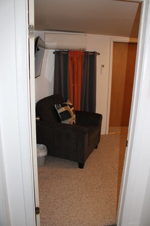 A room with a dark-colored sofa, a small table, and a wall-mounted air conditioning unit. - Cozy Creekside Retreat near Watkins Glen (Beaver Dams)