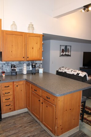 A kitchen with wooden cabinets, a granite countertop, and a coffee maker. - Cozy Creekside Retreat near Watkins Glen (Beaver Dams)
