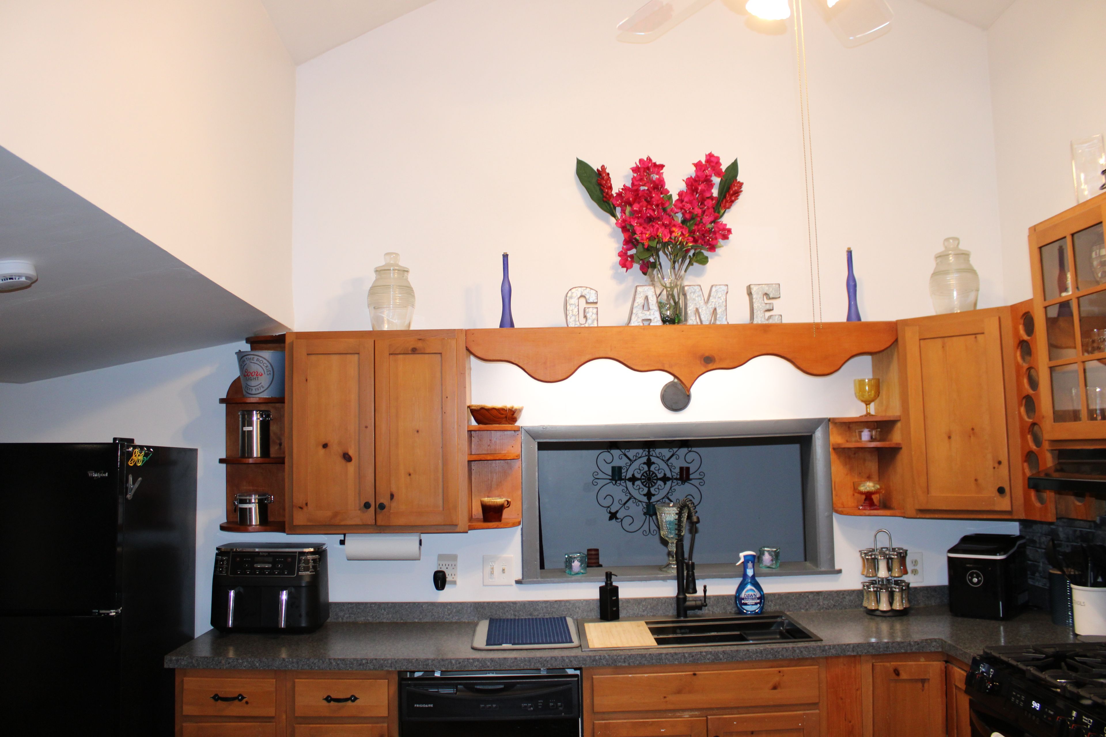 Cocina con armarios de madera, horno empotrado, lavavajillas y ventana con un salpicadero decorativo.