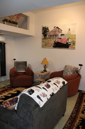 A living room with two armchairs, a sofa, a table with a lamp, and a painting of a barn on the wall. - Cozy Creekside Retreat near Watkins Glen (Beaver Dams)