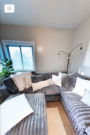 A modern living room with a large L-shaped sectional sofa, a small side table, and a floor lamp. - Vernal Sport Court Base Camp (Vernal)