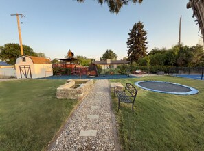 A backyard with a trampoline, a stone pathway, a bench, and a small shed.