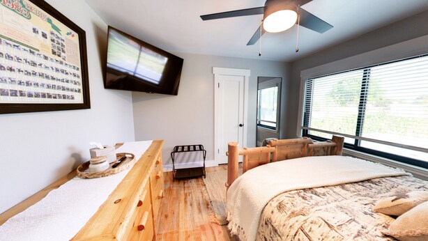 A bedroom with a bed, a wooden bench, a television mounted on the wall, and a window with blinds. - Vernal Sport Court Base Camp (Vernal)
