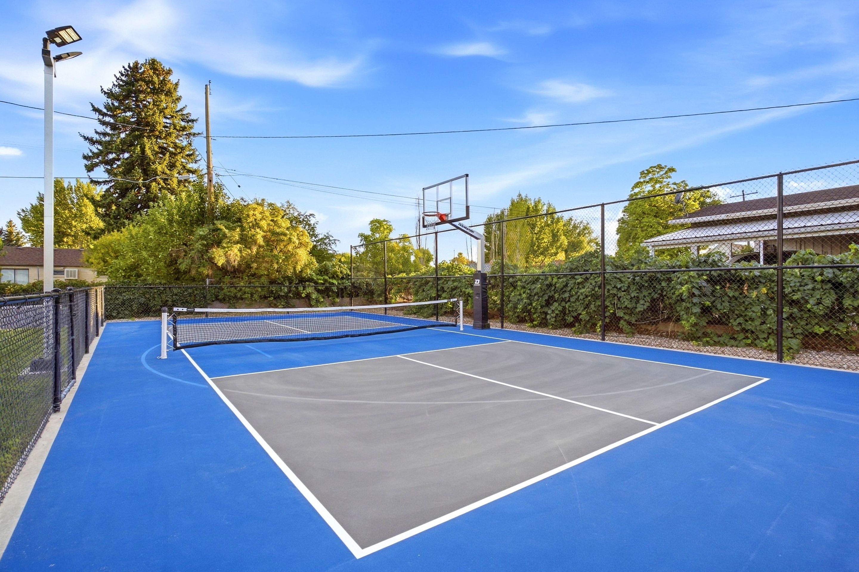 An outdoor tennis court with a net, surrounded by a fence and trees.