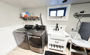 A laundry room with two front-loading washing machines, a white sink, and a window labeled 'LAUNDRY.'