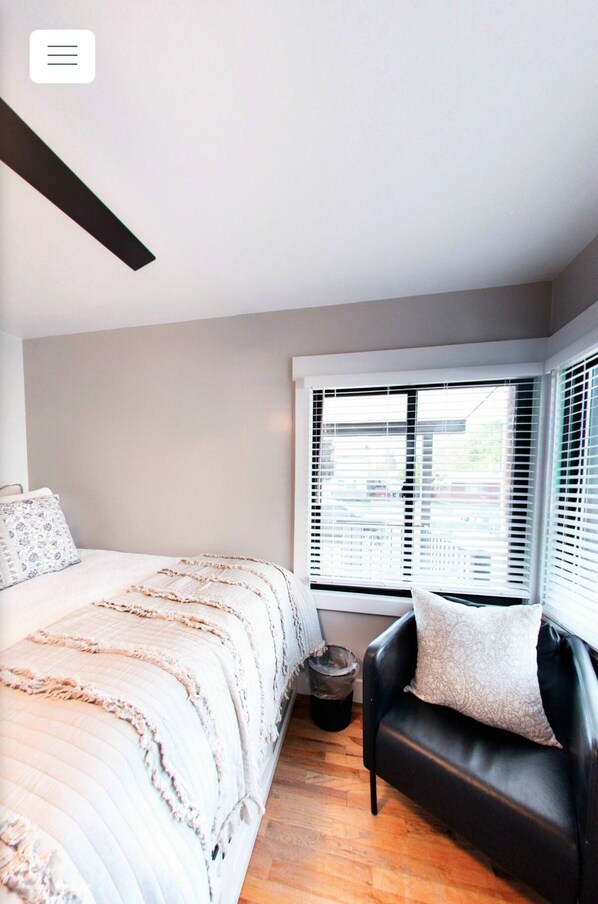 A bedroom with a bed, a black leather sofa, a window with blinds, and a ceiling light fixture. - Vernal Sport Court Base Camp (Vernal)