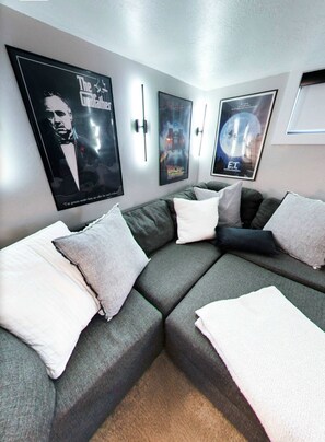 A modern living room with a sectional sofa, wall-mounted posters, and a window.