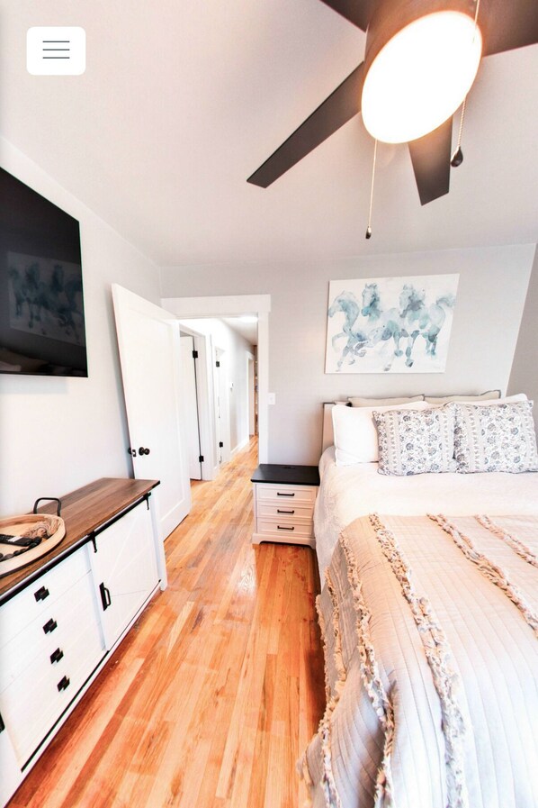 A bedroom with a bed, a dresser, a desk, and a ceiling fan.