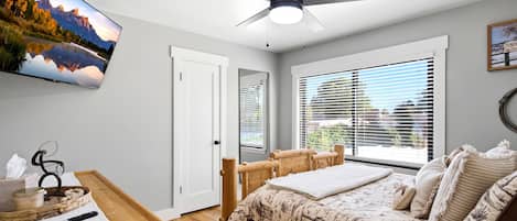 Une chambre à coucher comprenant un lit, un bureau, une chaise, un ventilateur de plafond et une fenêtre avec des stores.