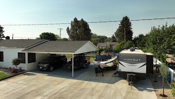 Un garage attenant à une maison, doté d’un abri de voiture couvert, d’une remorque pour bateau et d’une maison mobile portant l’inscription « HIDECUT ».