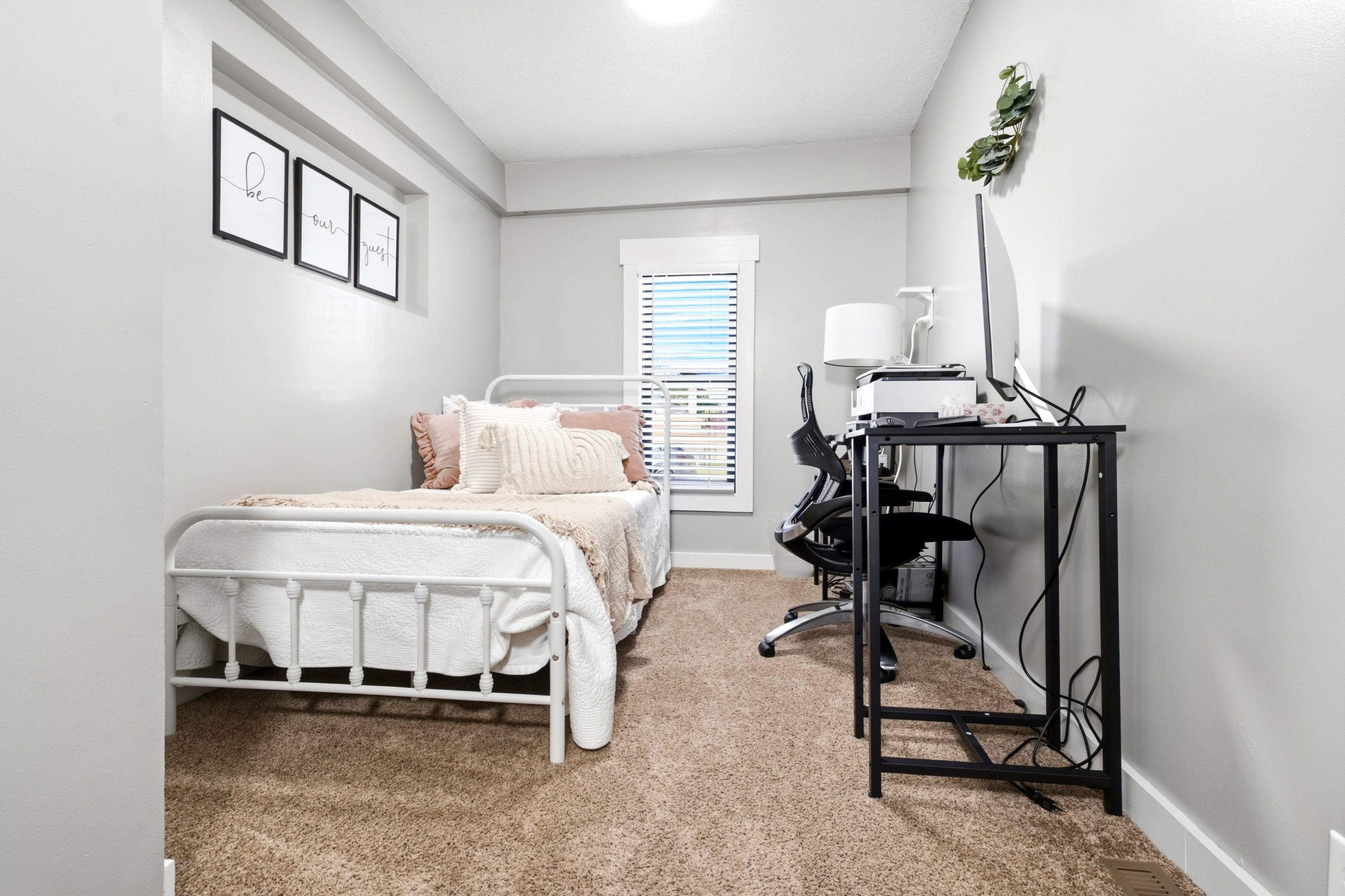 A bedroom with a bed, a desk, and a computer setup.