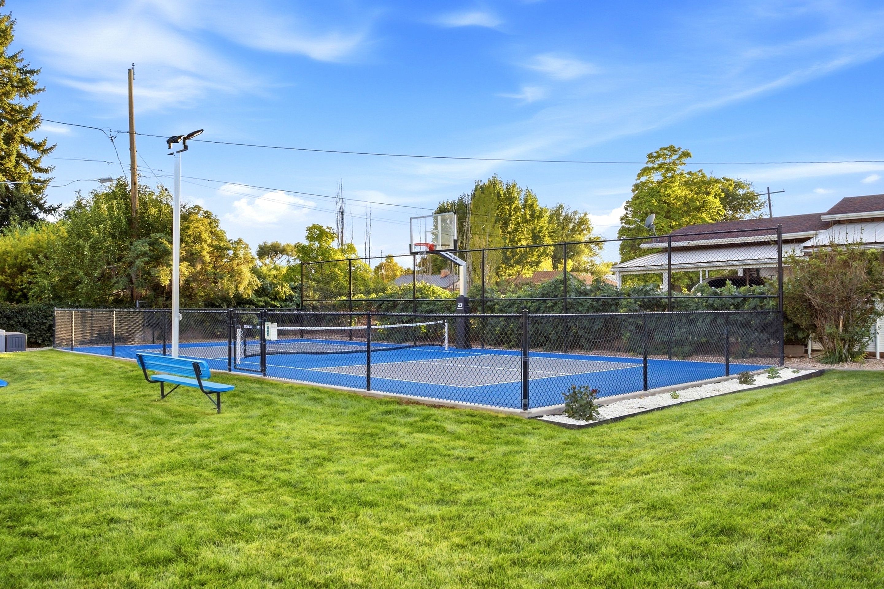 A fenced outdoor swimming pool with a blue deck, surrounded by a grassy area and trees.