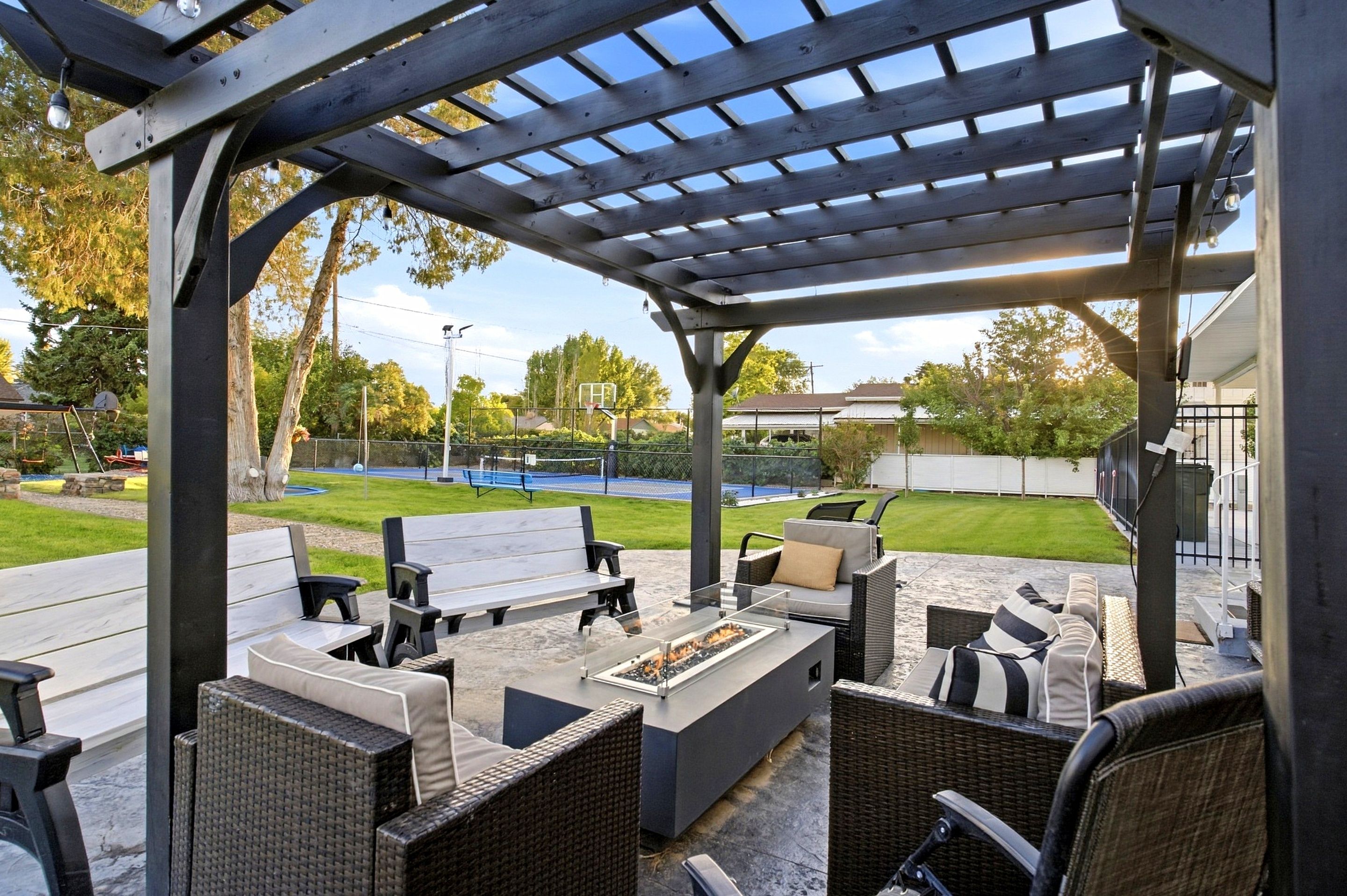 An outdoor patio with a pergola, seating area, and a fire pit.