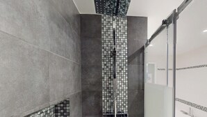 A modern bathroom with a shower, tiled walls, and a glass shower door. - Kimia Suite Room (Osny)