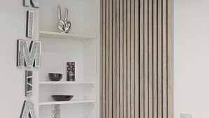 A kitchen with a microwave, shelves with kitchenware, and a decorative wall panel. - Kimia Suite Room (Osny)