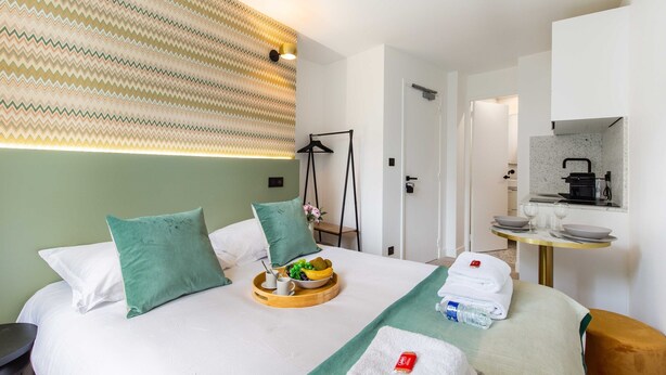 Ein Hotelzimmer mit einem Bett, einem Frühstücksbrett, einem Handtuch und einem kleinen Tisch mit Spiegel und Kaffeemaschine.
