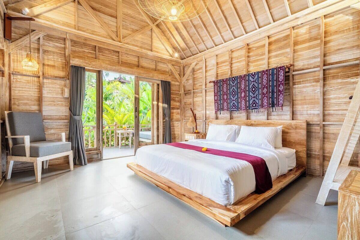 A wooden room with a bed, a chair, and a view of greenery outside.