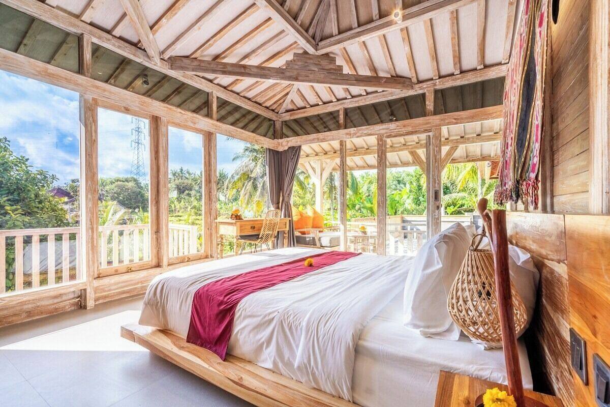 A spacious bedroom with a large bed, wooden beams, and a view of lush greenery.