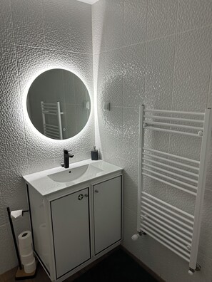 Ein Badezimmer mit einem weißen Waschbecken, einem runden Spiegel, einem Handtuchhalter und einem Toilettenpapierhalter.