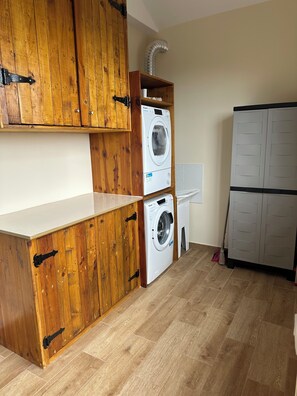 A laundry area with wooden cabinets, a washing machine, and a dryer. - Vila Romana (São Vicente, Segunda Lombada)