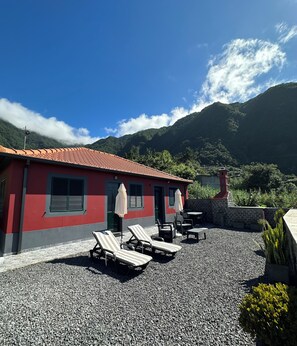 A red building with a tiled roof, outdoor seating with umbrellas, and a mountainous backdrop. - Vila Romana (São Vicente, Segunda Lombada)