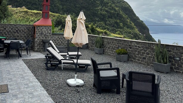 A terrace with lounge chairs, umbrellas, and a stone wall overlooking a mountainous landscape. - Unforgettable Madeira Stay! Near Levada Hikes! Ocean & Mountain Views! (São Vicente, Segunda Lombada)