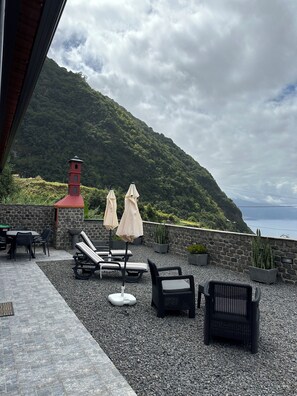 En terrasse med liggestole, parasoller og en stenvæg med udsigt over et bjergrigt landskab.