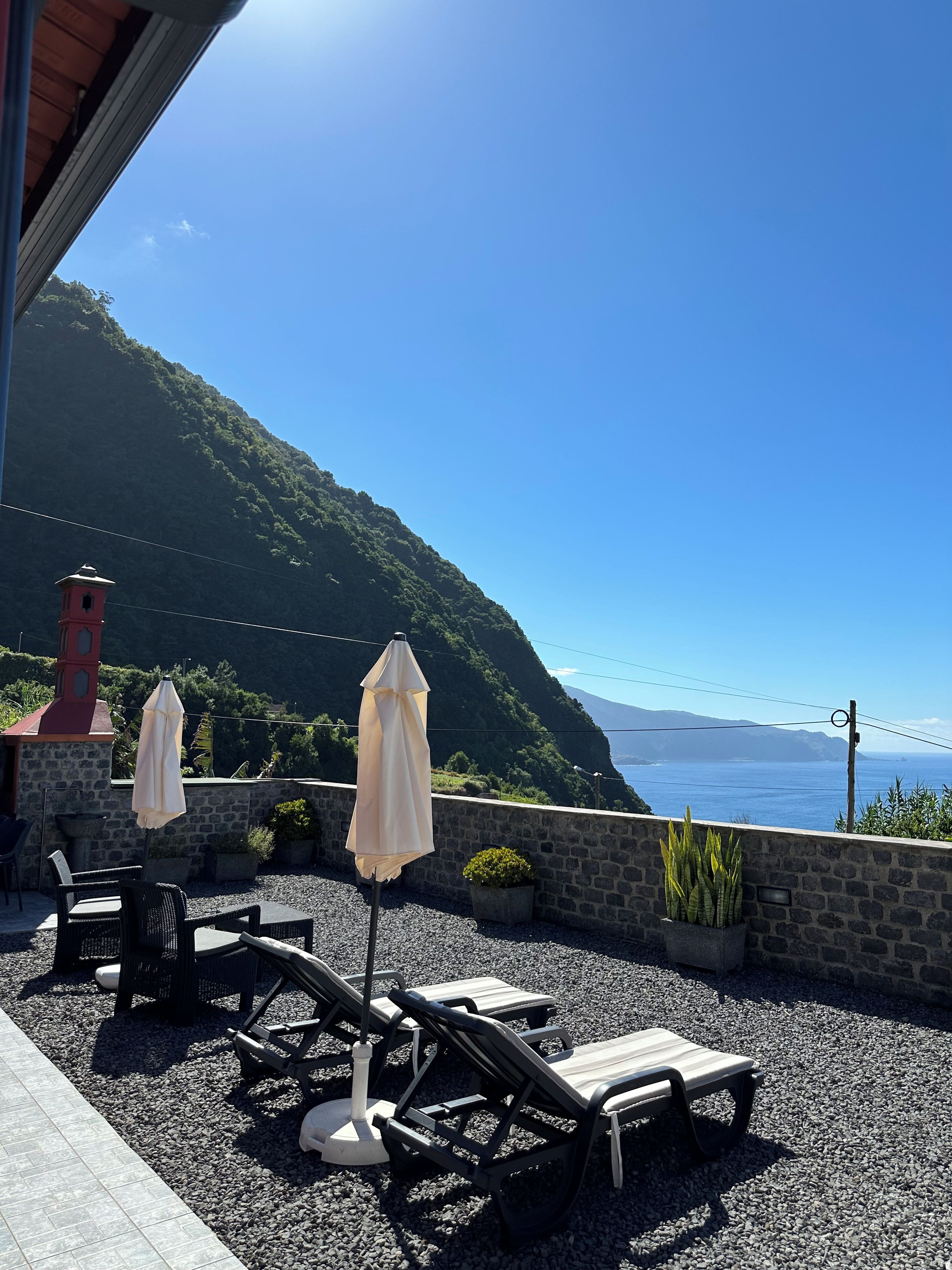Terraço com espreguiçadeiras e guarda-sóis com vista para a paisagem costeira.