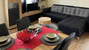 A modern living room with a black sofa, wooden coffee table, and a dining area with red placemats and plates. - Unforgettable Madeira Stay! Near Levada Hikes! Ocean & Mountain Views! (São Vicente, Segunda Lombada)