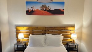 A hotel room with a large bed, two bedside lamps, a wooden headboard, a wall-mounted painting of a desert landscape, and a neatly made bed with folded towels. - Unforgettable Madeira Stay! Near Levada Hikes! Ocean & Mountain Views! (São Vicente, Segunda Lombada)