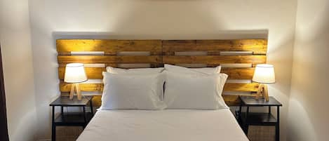 Une chambre d’hôtel avec un grand lit, deux lampes de chevet, une tête de lit en bois, un tableau représentant un paysage désertique accroché au mur, et un lit parfaitement fait avec des serviettes pliées.