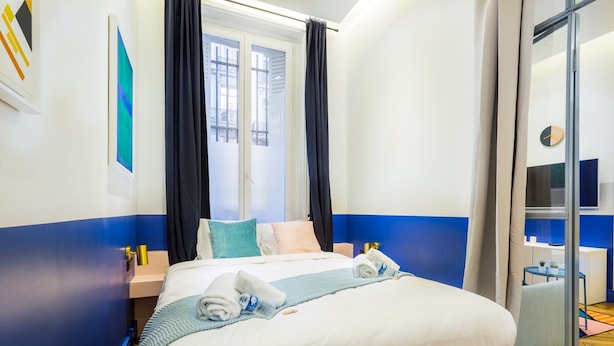 Una habitación de hotel con cama, ventana con cortinas, televisión y una pequeña mesa con una planta.