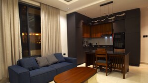 Una sala de estar moderna con un sofá azul, una mesa de comedor de madera y una cocina con armarios oscuros y una estufa.