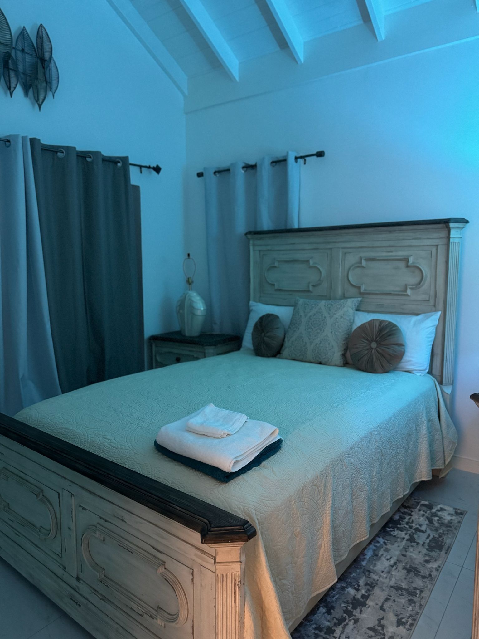 Een slaapkamer met een bed, gordijnen, een nachtkastje en een decoratief wandobject.