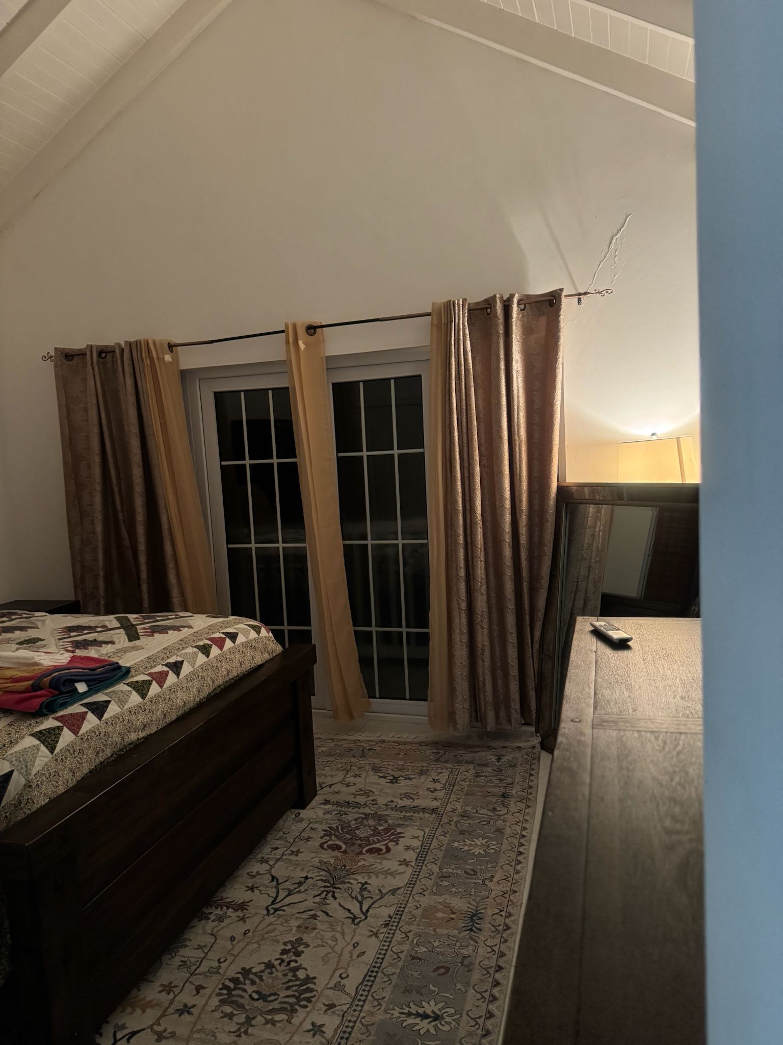 A bedroom with a bed, a nightstand, a dresser, a window with curtains, and a lamp.