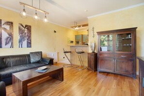 Una sala de estar con sofá, una mesa de centro y taburetes de bar. Se observa un mueble de madera y una zona de cocina al fondo.