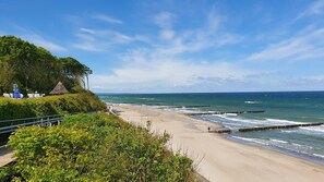 A beach with a wooden pier, a thatched-roof structure, and lush greenery. - Apartment 'Am Gespensterwald' with Private Terrace (Nienhagen)